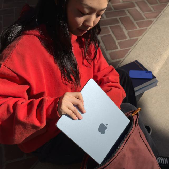 Person placing sky blue MacBook Air into their bag
